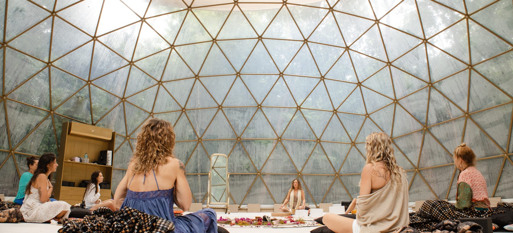 Women seated in circle inside the geodesic dome, Anya at the centre beside the flower mandala