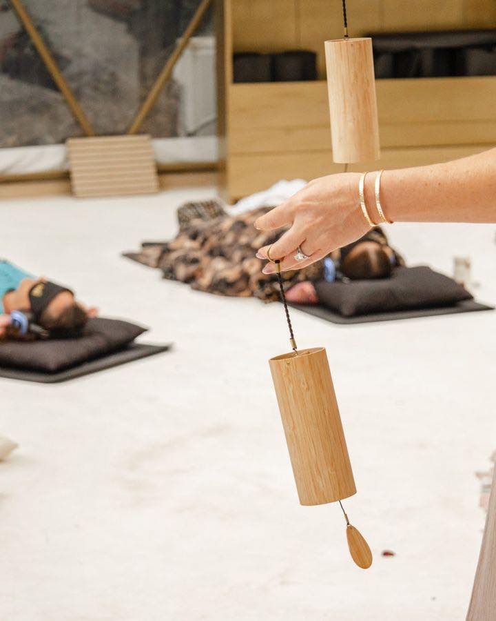 Anya Dillon playing a bamboo chime above guests resting on their mats