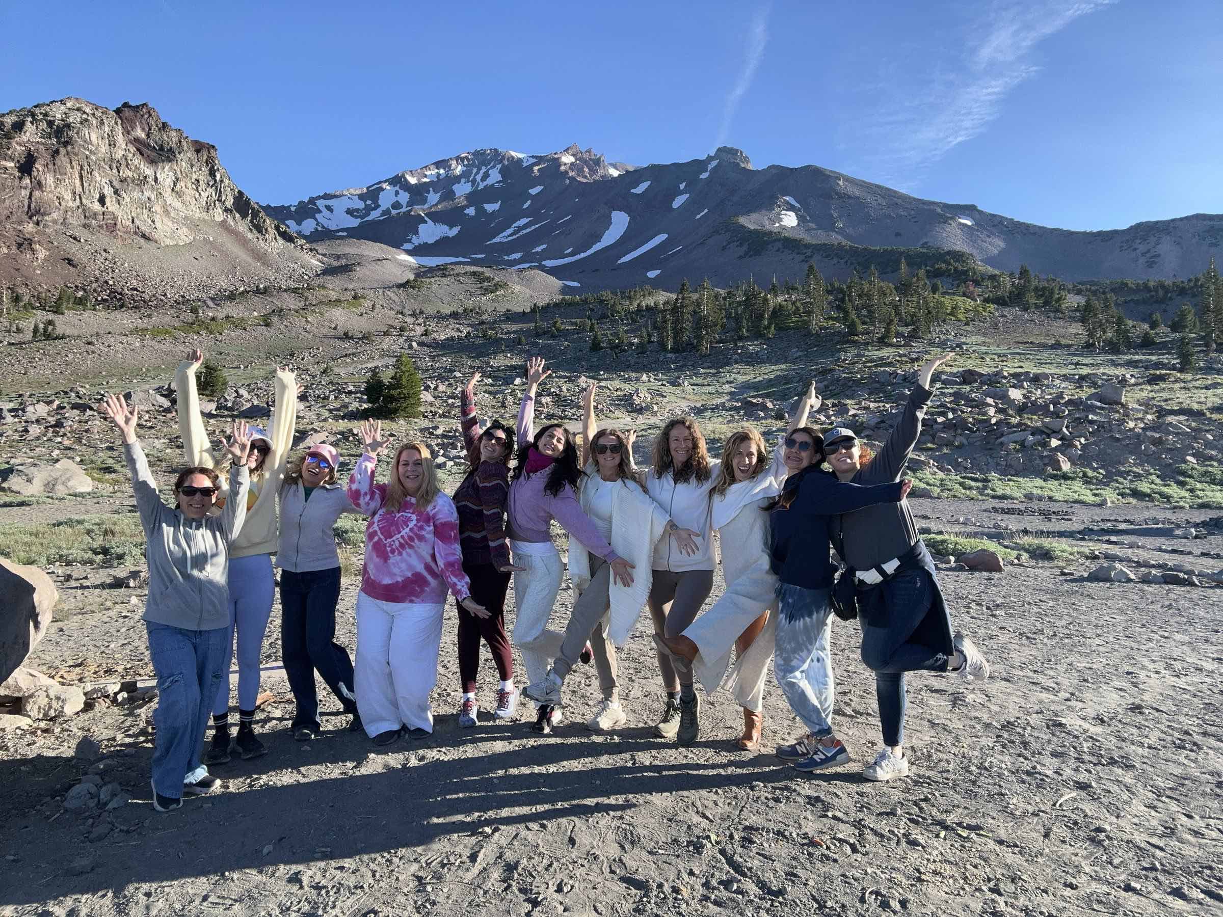 The Cosmic Remembrance circle with arms raised in celebration, standing together beneath the snowy peak of Mount Shasta