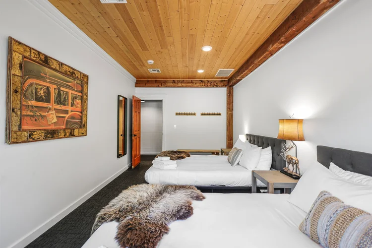 Two queen beds beneath a warm pine ceiling, sheepskin throws at the foot of each