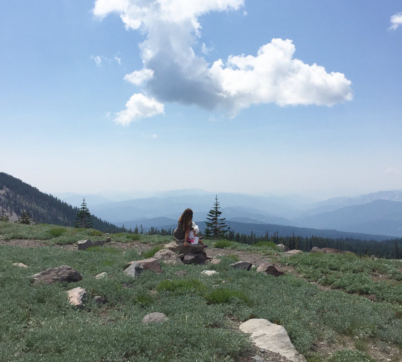 A woman sitting alone on the mountainside beneath a single cloud